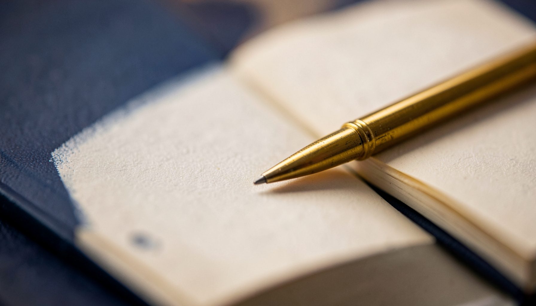 Gros plan sur un cahier ouvert avec un stylo doré posé dessus, tons chauds et neutres
