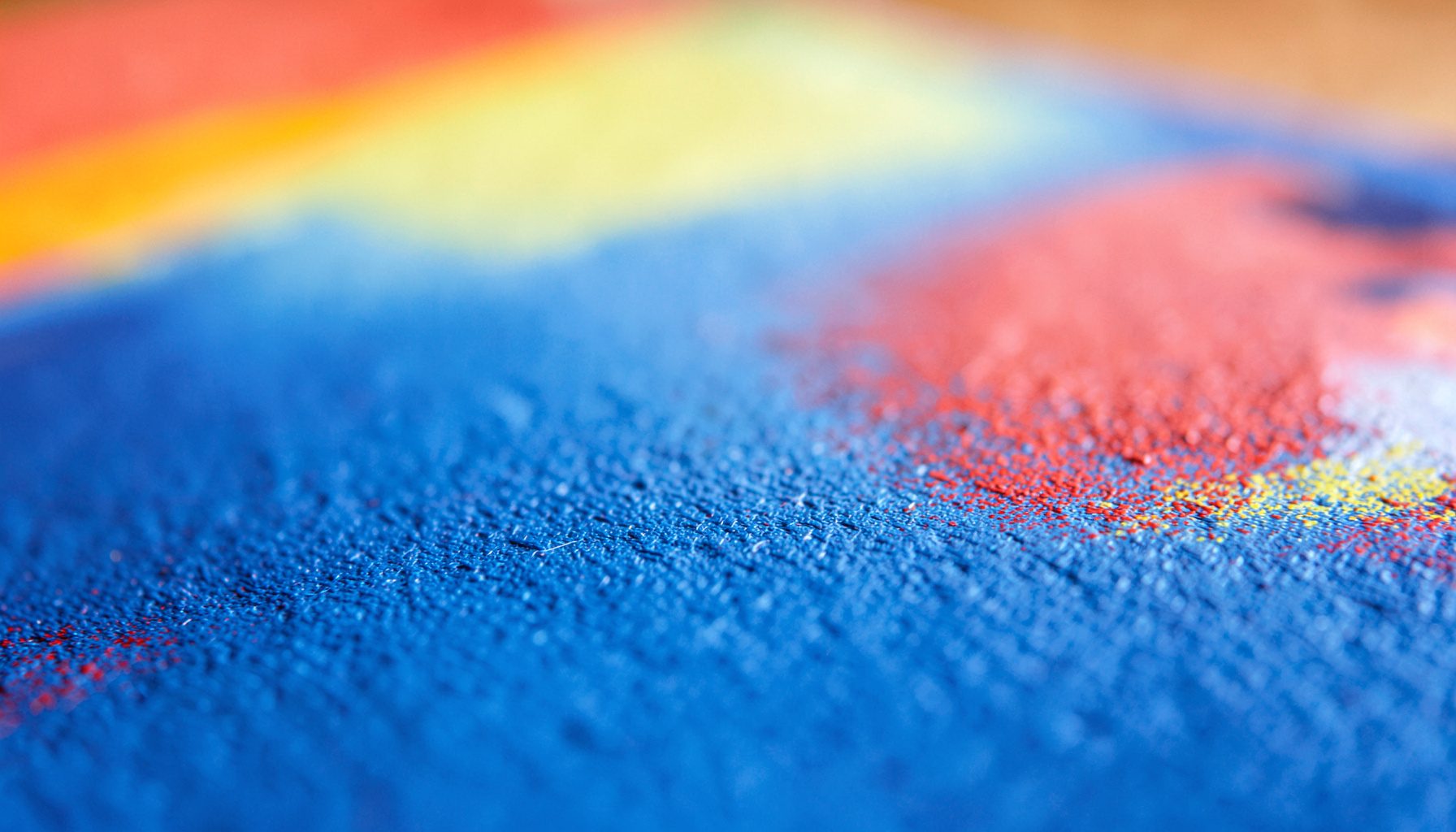 Gros plan extrême d'une page de livre pour enfants aux couleurs vives, où l'on distingue la texture du papier légèrement granuleux et des touches de rouge, de jaune et de bleu qui se fondent dans un arrière-plan doux et chaleureux.