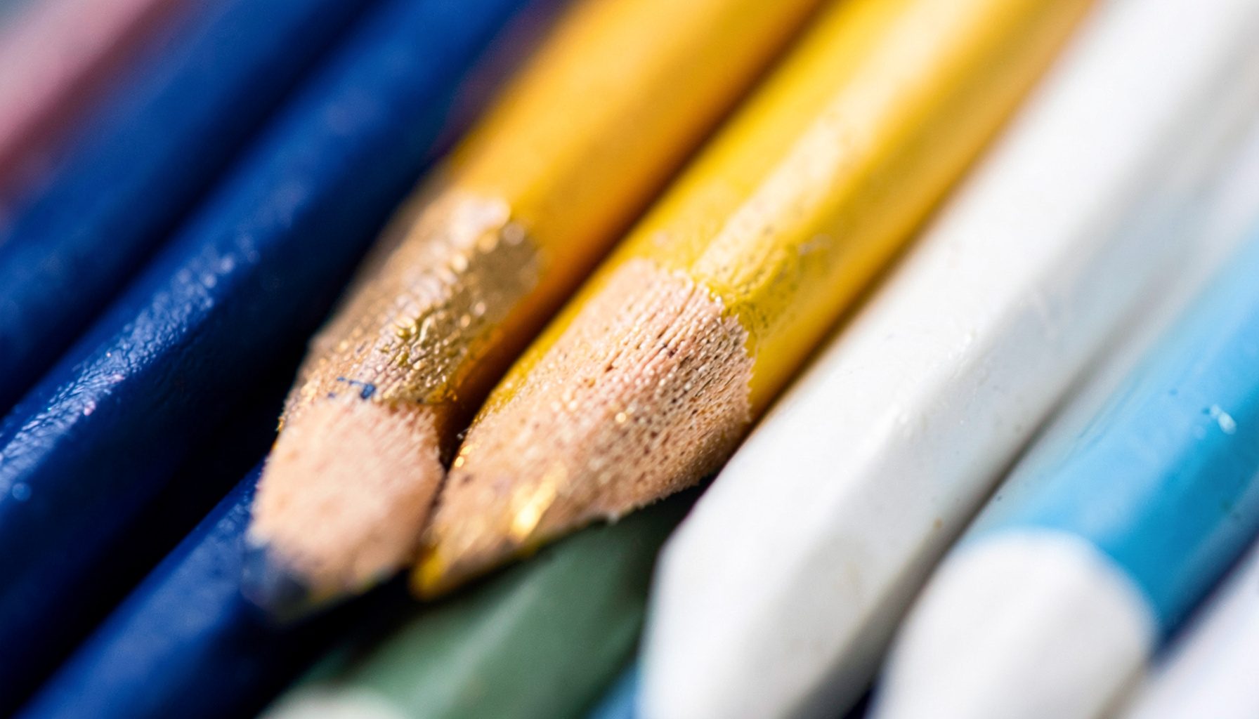Gros plan sur des crayons de couleur alignés, tons bleu marine, jaune doré et blanc, ambiance ludique
