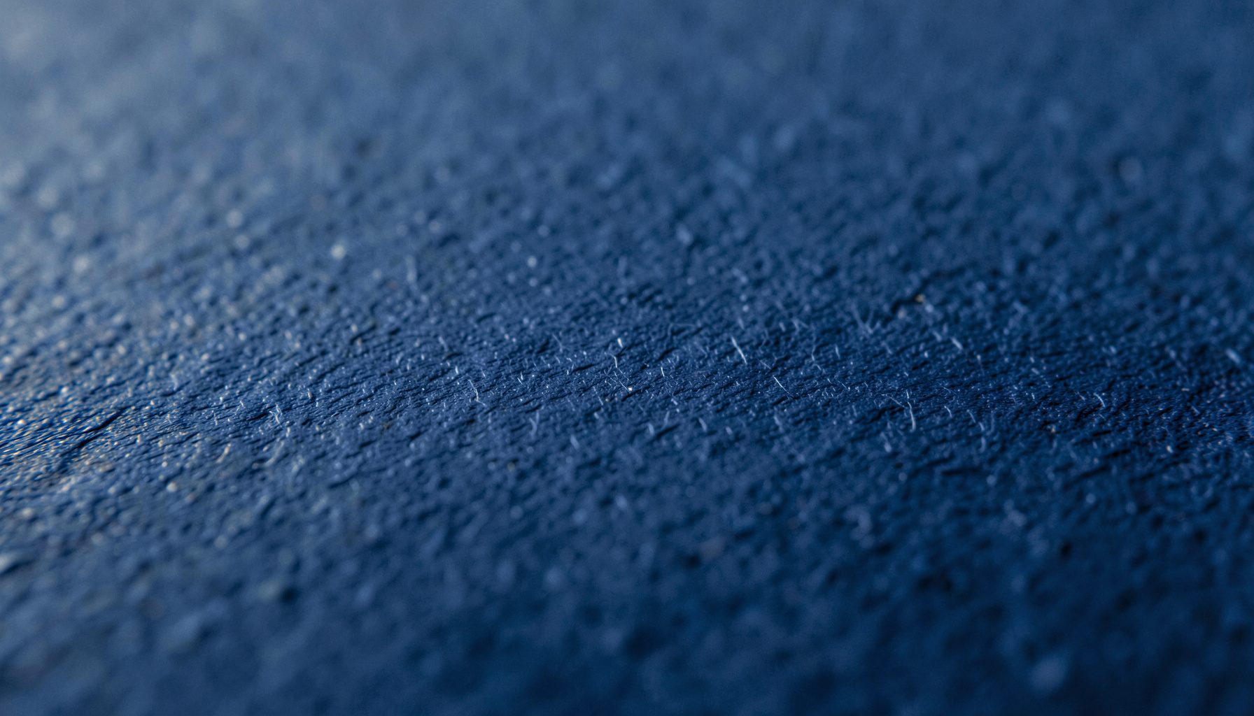 Gros plan extrême d'une texture de papier cartonné bleu marine, surface légèrement grainée avec des micro-fibres visibles, éclairage doux et chaleureux.